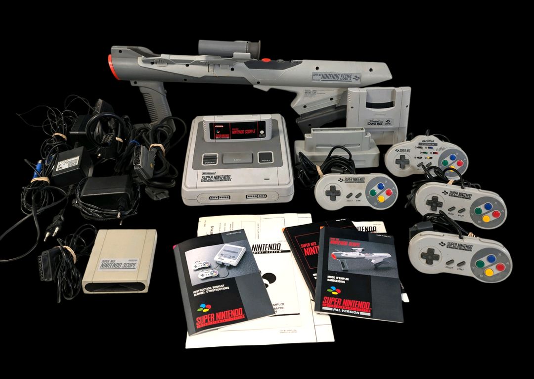 Nintendo – Lot conséquent comprenant : – Console de salon Super Nes. Test d&rsquo;allumage effectué avec succès. – Jeu associé : Super Nintendo Scope 6. Avec Le Super Nintendo Scope, son détecteur SNES, 4 manettes dont 3 officielles, notices de la Super Nes et notices du Super Scope,, dépliant, un Super Nes European Adaptator, un adaptateur Super GameBoy, cordon d&rsquo;alimentation, câble péritel ainsi que d&rsquo;autres câbles divers.